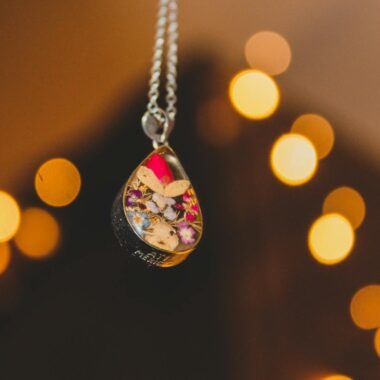 A close-up of a handmade pendant with flowers and leaves, featuring a warm bokeh background.