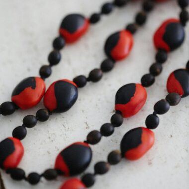 Close-up of a handmade black and red clay bead necklace on a light surface, showcasing its artistic design.