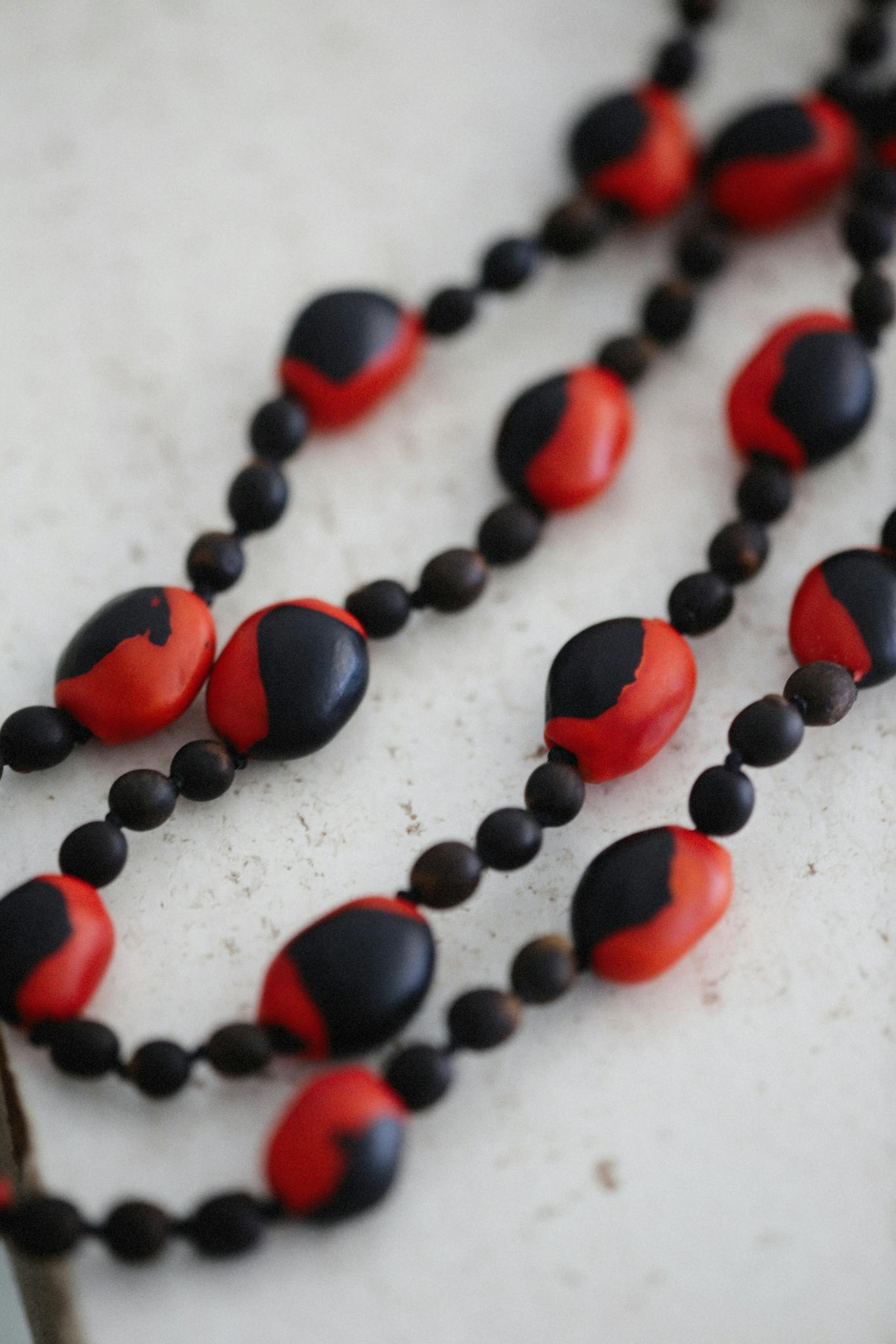 Close-up of a handmade black and red clay bead necklace on a light surface, showcasing its artistic design.