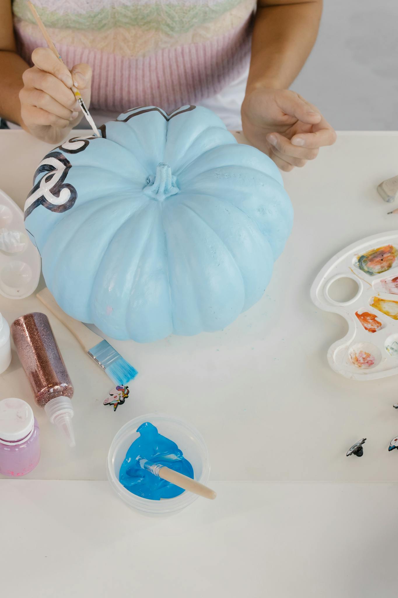 Close-up of painting a blue pumpkin with art materials for Halloween decor.