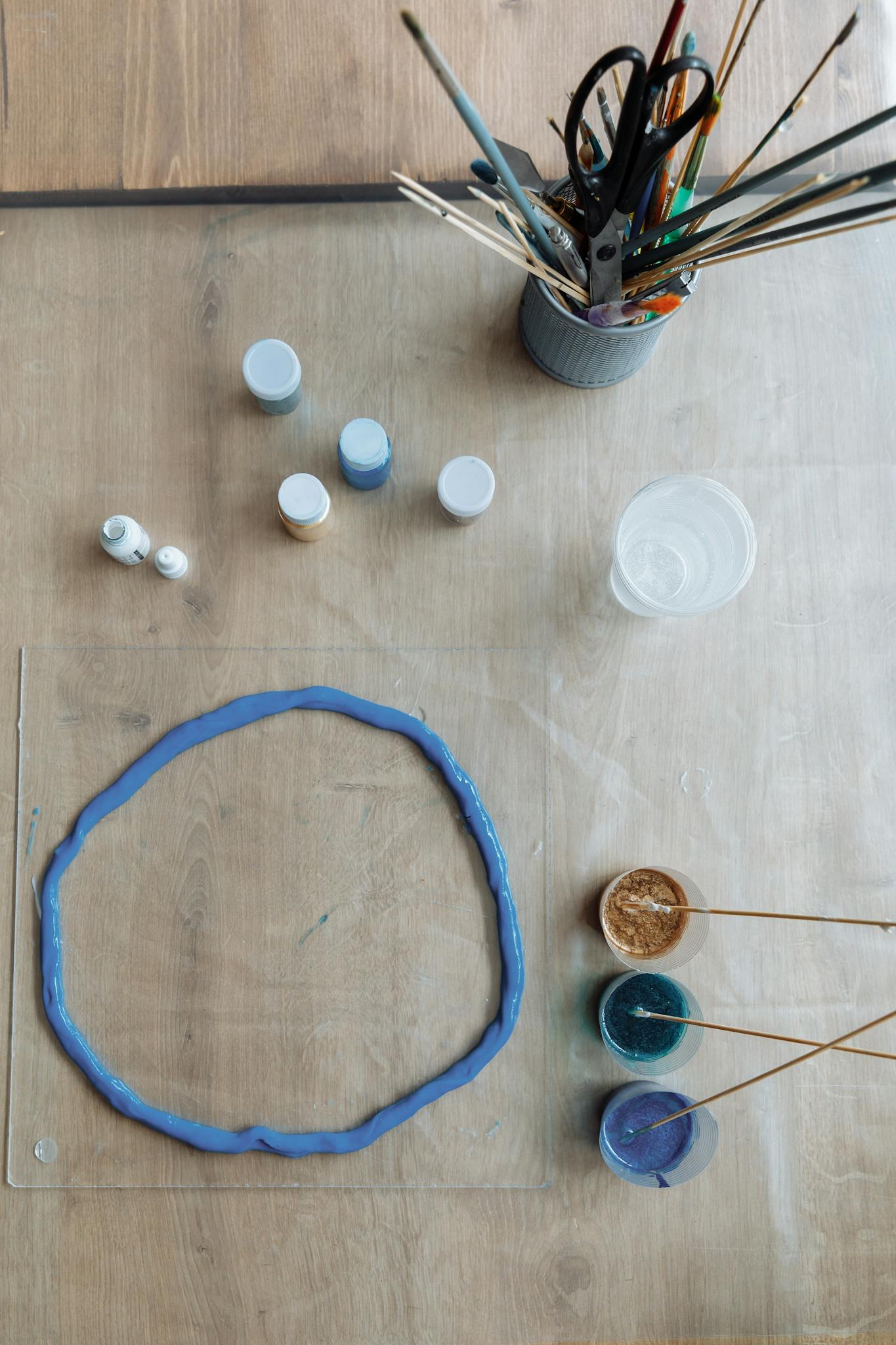 Top view of resin art supplies on a wooden table, showcasing paints and brushes.